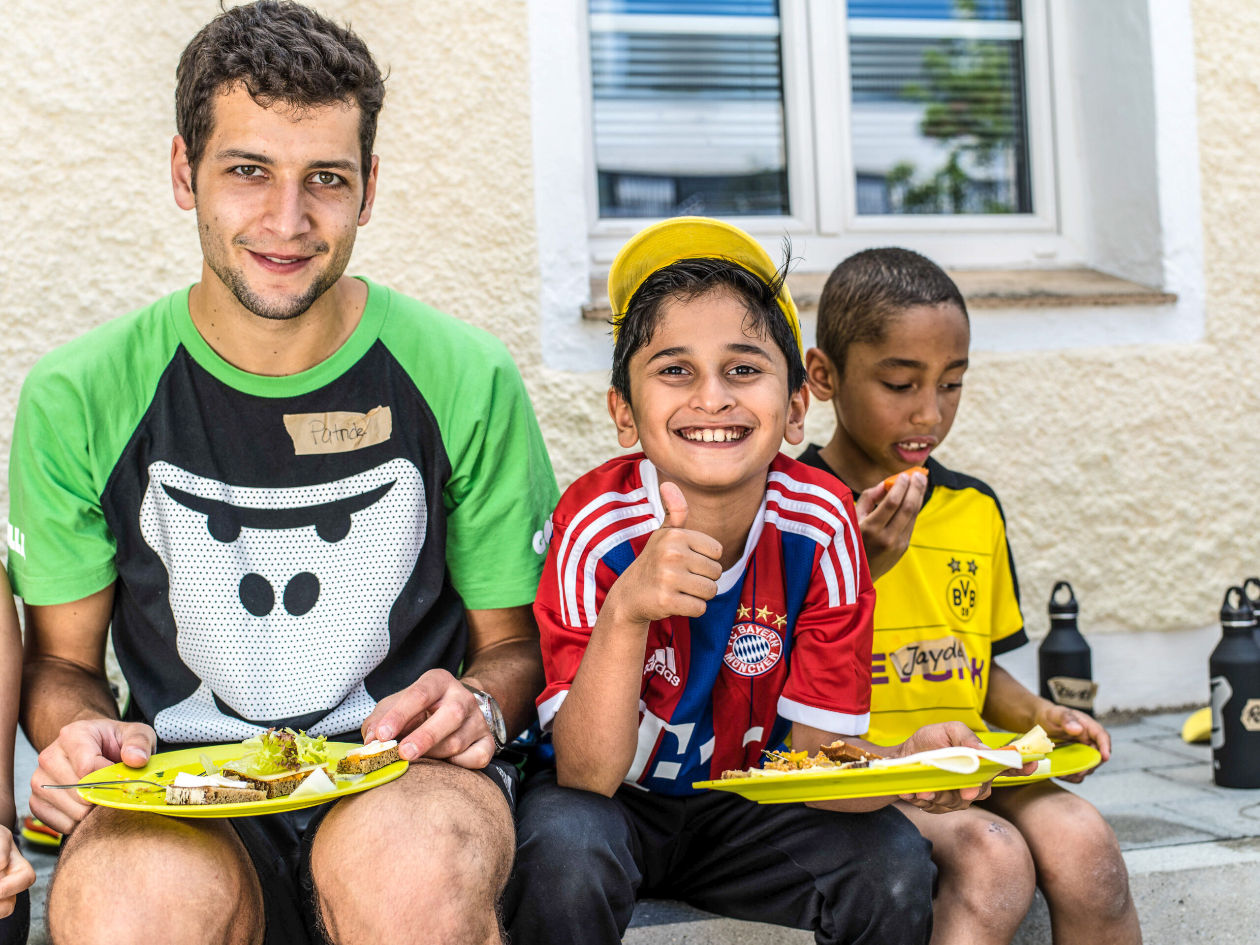 Ein GORILLA Botschafter und ein Kind essen voller Freude ihr Mittagessen im Rahmen eines GORILLA Workshops. Der Junge macht den Daumen hoch als Zeichen seiner Freude.