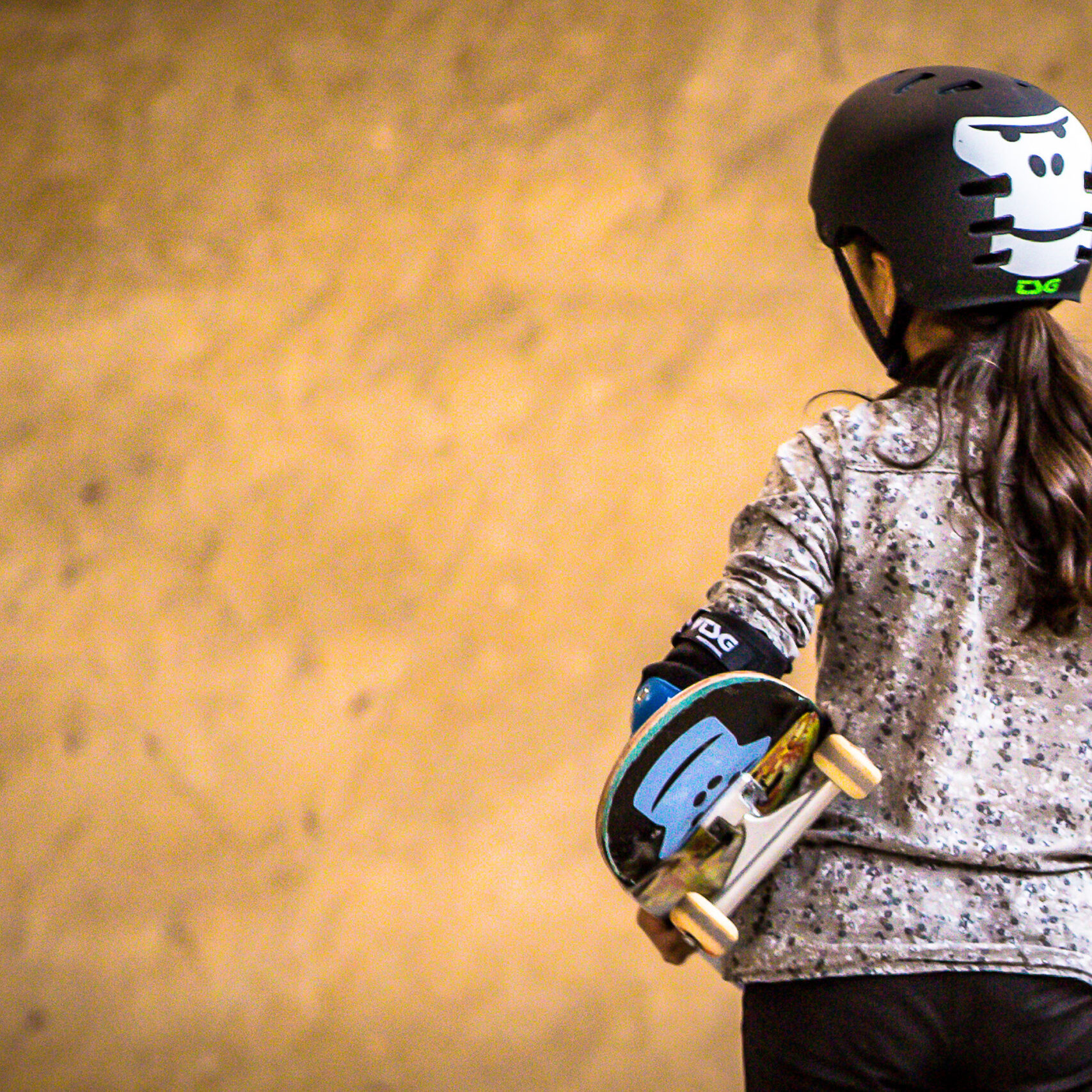 Ein Maedchen von hinten mit GORILLA Helm und Skateboard im Rahmen eines GORILLA Workshops in einem Skatepark.