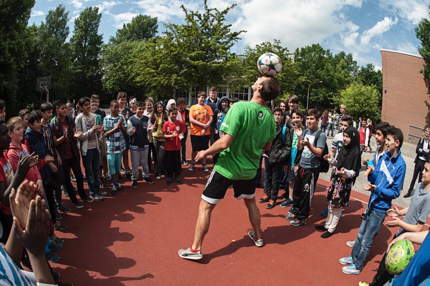 GORILLA Botschafter macht in einem Kreis von begeisterten Kindern einen Trick indem er mit dem Kopf einen Fußball jongliert.