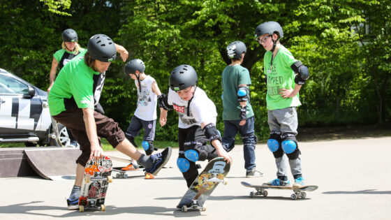 GORILLA Botschafter Tobias Kupfer zeigt 2 Jungen wir man einen Trick auf dem Skateboard macht.